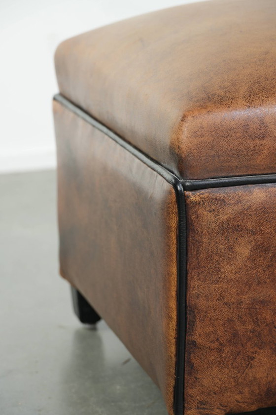 Image 1 of Characterful sheepskin footstool/ottoman with a beautiful patina and finished with black piping.