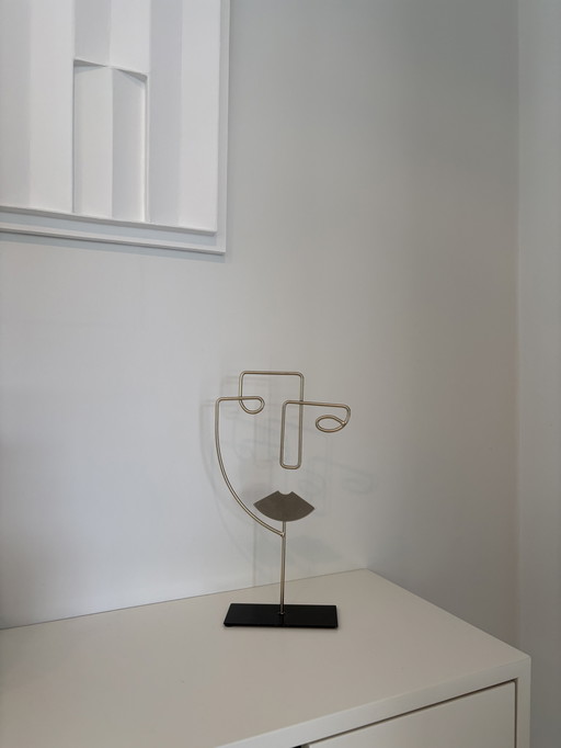 Modern wire sculpture of a stylized face, in gold color