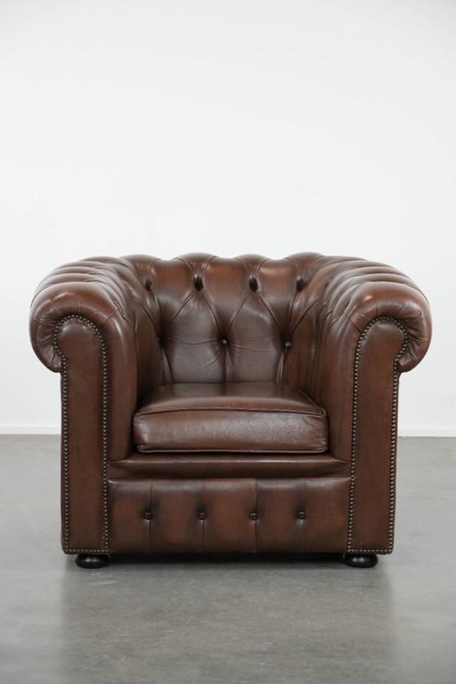 Impresionante sillón Chesterfield de piel de vaca marrón al estilo inglés, acabado con clavos decorativos.