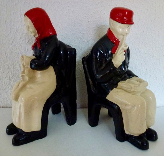 Image 1 of A set of decorative bookends depicting an elderly couple sitting on chairs.