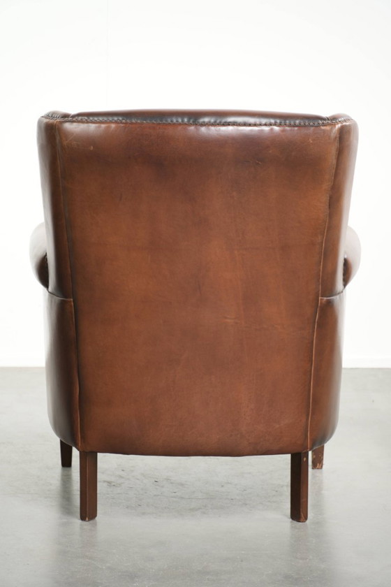 Image 1 of Precioso sillón orejero de piel de oveja marrón oscuro con un aspecto atemporal en un tamaño sutil.