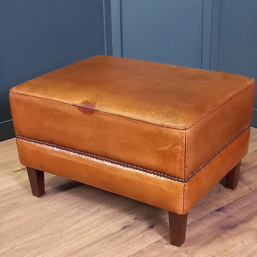Caratteristico poggiapiedi/pouf in pelle di pecora con una splendida patina e rifinito con borchie decorative.