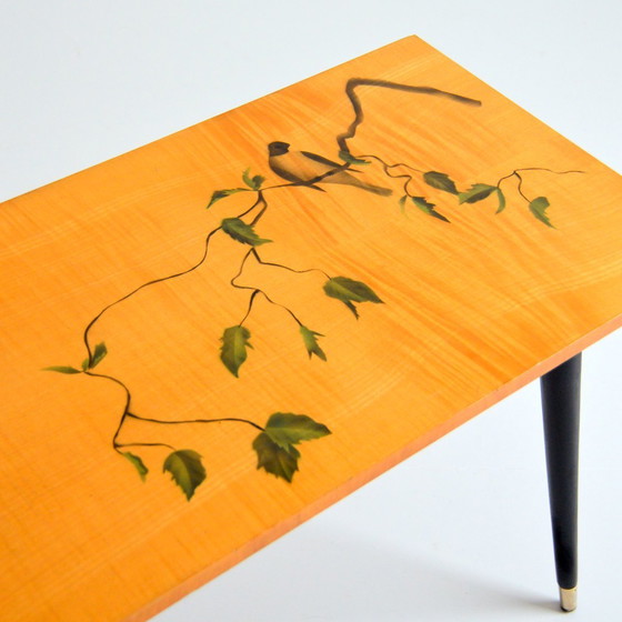 Image 1 of Pretty coffee table from the 50s/60s.  Decorated with a bird on a branch.  Black brass-finish tapered legs.  L 80/ W 40/ H 51