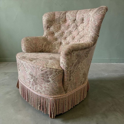 Sillón individual vintage rosa claro con estampado floral y flecos.