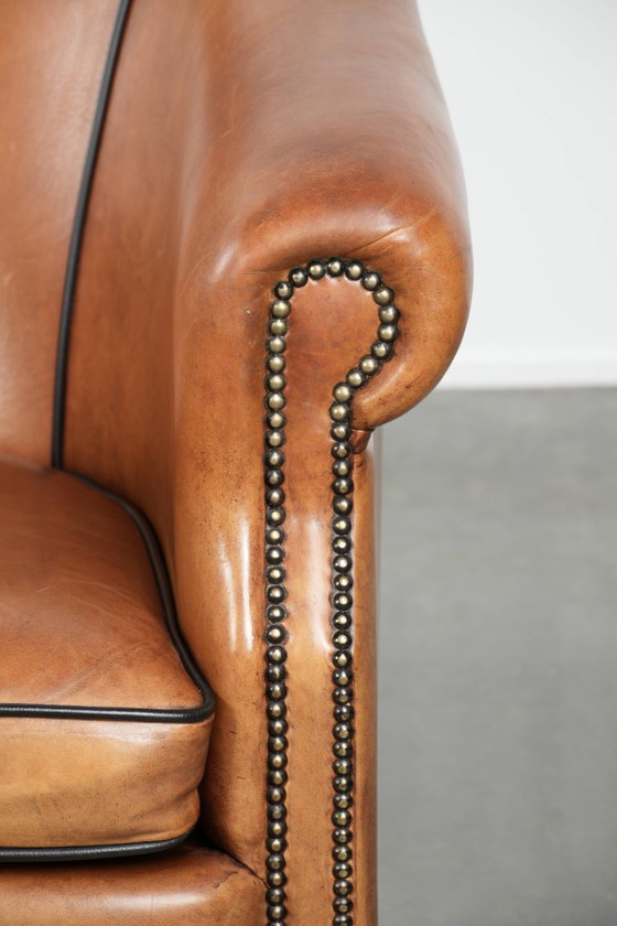 Image 1 of Amplio sillón club de estilo inglés, tapizado en piel de oveja, con acabado de clavos decorativos y ribetes negros.