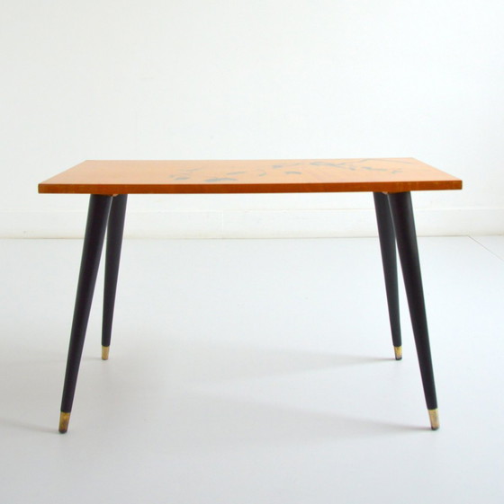 Image 1 of Pretty coffee table from the 50s/60s.  Decorated with a bird on a branch.  Black brass-finish tapered legs.  L 80/ W 40/ H 51