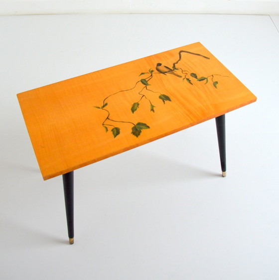 Image 1 of Pretty coffee table from the 50s/60s.  Decorated with a bird on a branch.  Black brass-finish tapered legs.  L 80/ W 40/ H 51