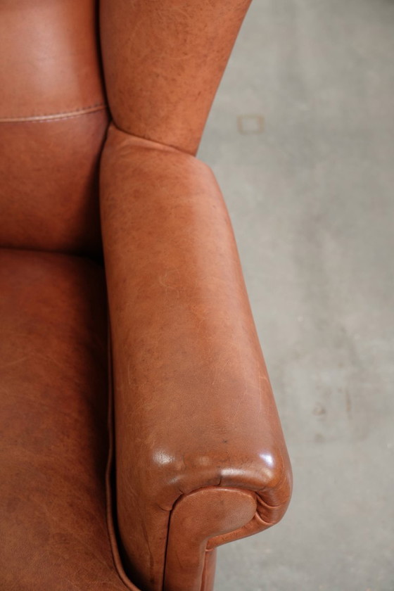 Image 1 of Fauteuil à oreilles en cuir de vachette couleur cognac clair, avec passepoil assorti et un style anglais plein de caractère.