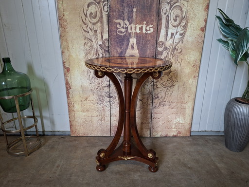 Mesa central redonda clásica de chapa de nogal con marquetería, base ornamentada y herrajes de latón.