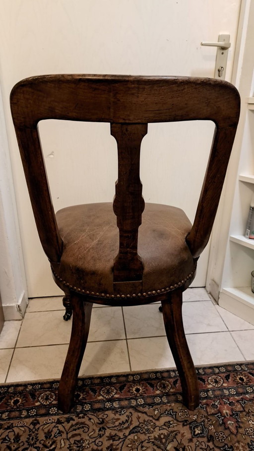 Silla antigua de madera con tapizado de cuero y clavos decorativos.