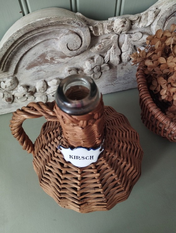 Image 1 of Kleine glazen demijohn, geweven rieten envelop, Kirsch emaille etiket
