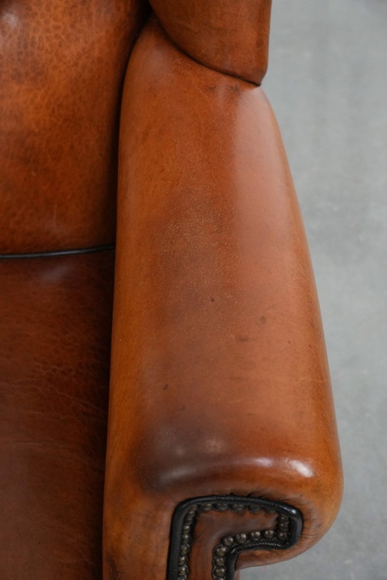 Image 1 of Grote oorfauteuil gemaakt van schapenleer met zwarte biezen en siernagels