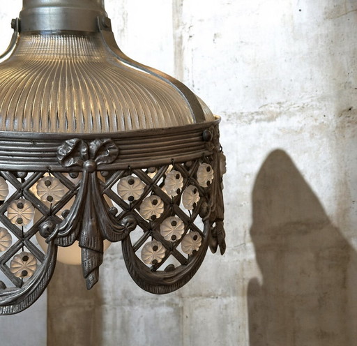Dit is een antieke of vintage Holophane hanglamp met een geribbeld glazen kap en een gedetailleerde metalen rand. 