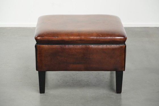 Image 1 of Grote donkerbruine vierkante hocker gemaakt van schapenleer met zwarte biezen