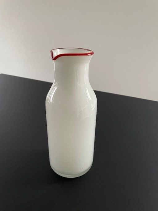 Caraffa dal design scandinavo in vetro bianco con bordo rosso.