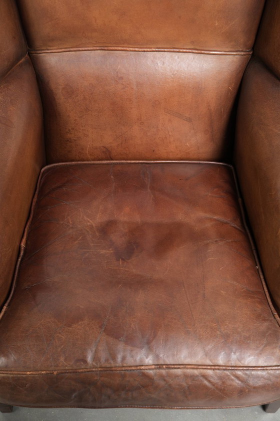 Image 1 of Precioso sillón orejero de piel de oveja marrón oscuro con un aspecto atemporal en un tamaño sutil.