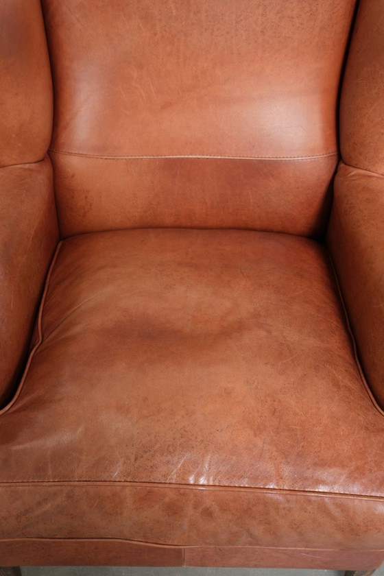 Image 1 of Fauteuil à oreilles en cuir de vachette couleur cognac clair, avec passepoil assorti et un style anglais plein de caractère.