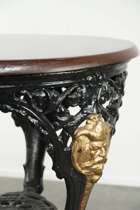 Image 1 of Antieke Engelse bistro/ bijzettafel met een gietijzeren onderstel uit begin 20e eeuw en een massief houten tafelblad