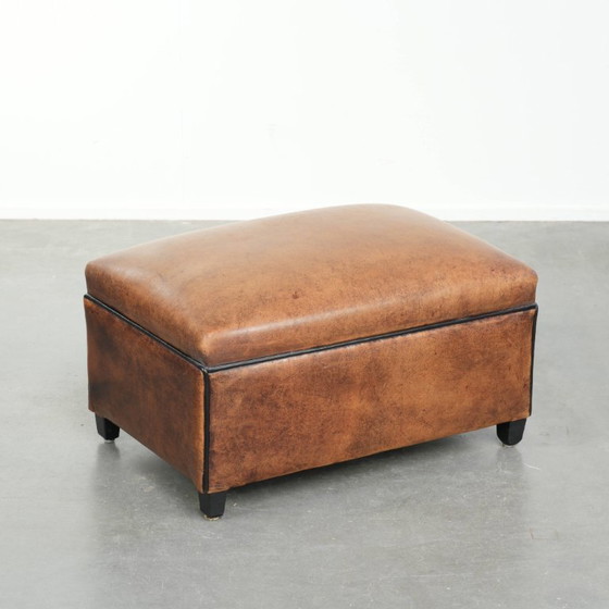 Image 1 of Characterful sheepskin footstool/ottoman with a beautiful patina and finished with black piping.
