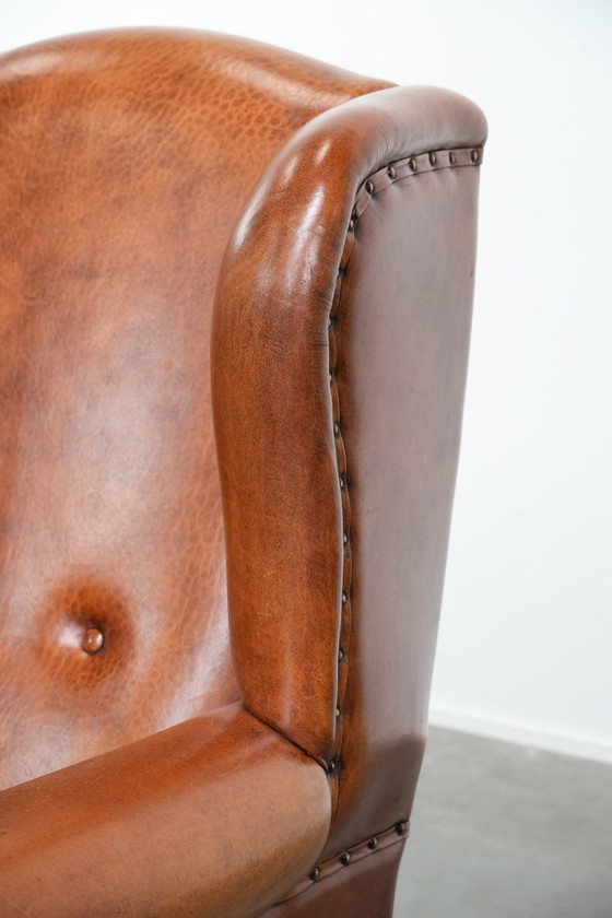 Image 1 of Grote oorfauteuil gemaakt van schapenleer met zwarte biezen en siernagels