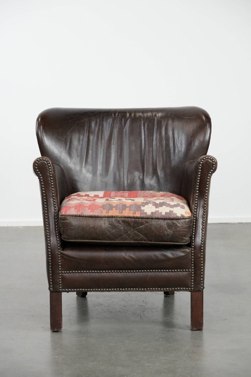 Subtiele donkerbruine fauteuil gemaakt van rundleer met een omkeerbaar Kelim zitkussen