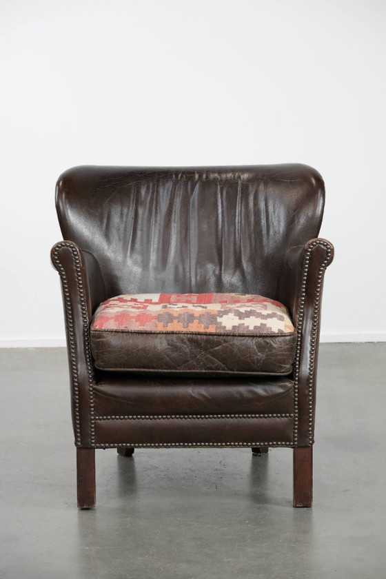 Image 1 of Subtiele donkerbruine fauteuil gemaakt van rundleer met een omkeerbaar Kelim zitkussen