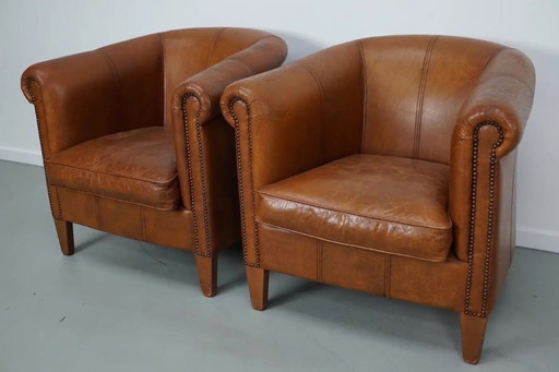 Dit paar cognackleurige leren clubfauteuils komt uit Nederland. Ze zijn bekleed met cognackleurig leer en zijn voorzien van meta