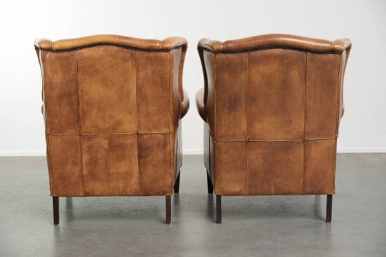 Image 1 of Dos hermosos sillones orejeros de piel de vaca clara con un estilo inglés atemporal y gran comodidad.
