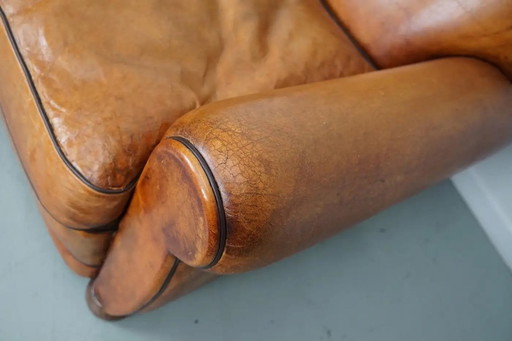 Sillón club francés vintage de cuero color coñac con respaldo en forma de bigote.