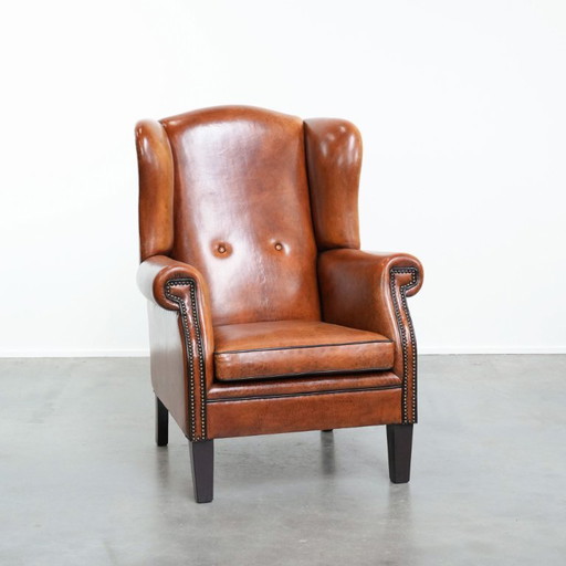 Grote schapenleren oorfauteuil met zwarte biezen en siernagels