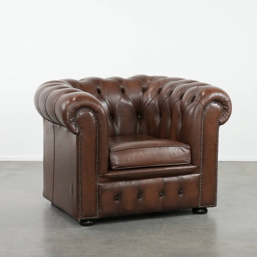 Impresionante sillón Chesterfield de piel de vaca marrón al estilo inglés, acabado con clavos decorativos.