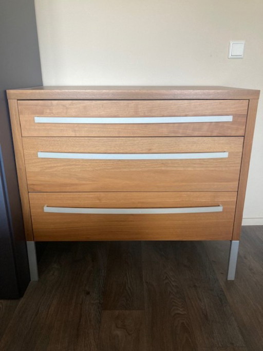 Cómoda vintage IKEA MALM con tres cajones, acabado en chapa de madera, tiradores y patas de color plateado.