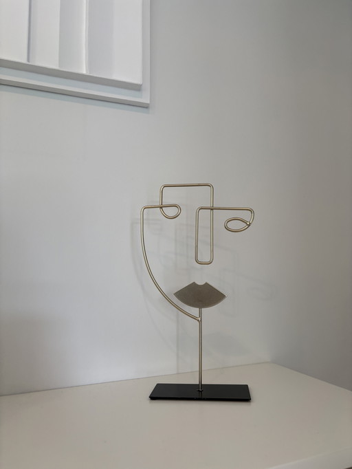 Modern wire sculpture of a stylized face, in gold color