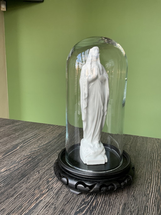 Estatua de porcelana de la Virgen María bajo una cúpula de cristal.