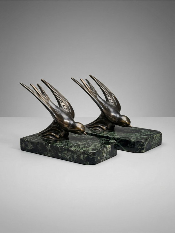 Image 1 of Een paar art-deco boekensteunen – zwaluwen van gepatineerd zink op groene marmeren voetstukken.