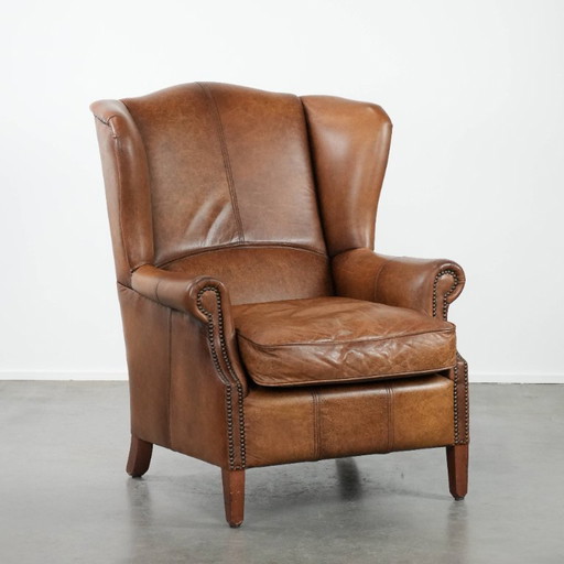 Tijdloze cognac kleurige oorfauteuil in Engelse stijl gemaakt van rundleer afgewerkt met siernagels