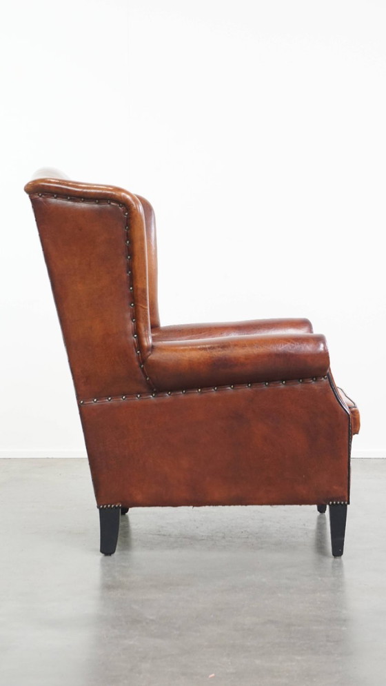 Image 1 of Schapenleren oorfauteuil met een warme kleurstelling en een afwerking met siernagels en zwarte biezen