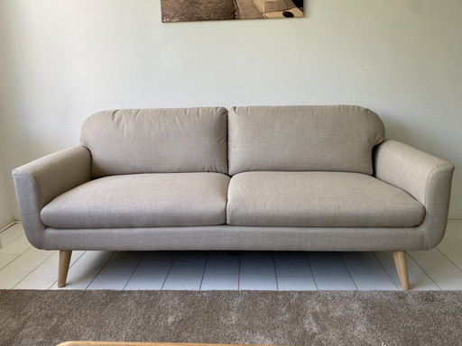 Elegante sofá de 3 plazas con tapicería de tela beige y patas de madera.