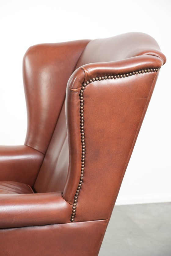 Image 1 of Comoda poltrona a orecchioni in pelle bovina color cognac in stile inglese.