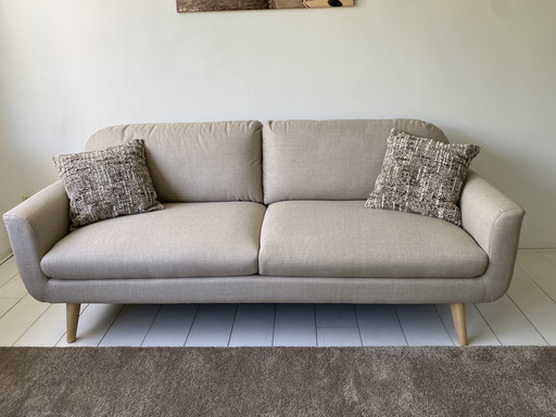 Elegante sofá de 3 plazas con tapicería de tela beige y patas de madera.