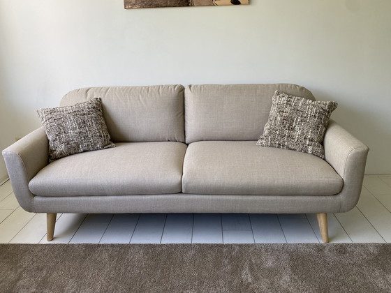 Image 1 of Elegante sofá de 3 plazas con tapicería de tela beige y patas de madera.
