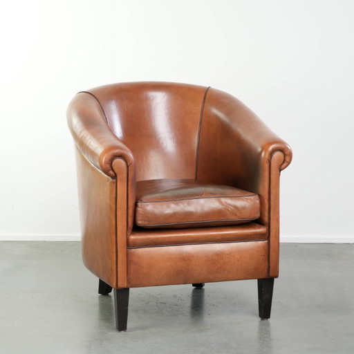 Vintage schapenleren clubfauteuil met een warme kleurstelling en afgewerkt met zwarte biezen