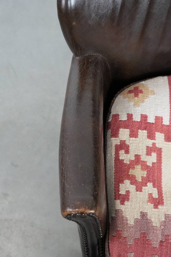 Image 1 of Subtiele donkerbruine fauteuil gemaakt van rundleer met een omkeerbaar Kelim zitkussen