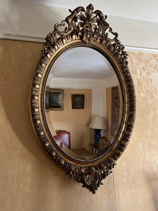 Antieke ovale spiegel met verguld stucwerk en ornamenten.