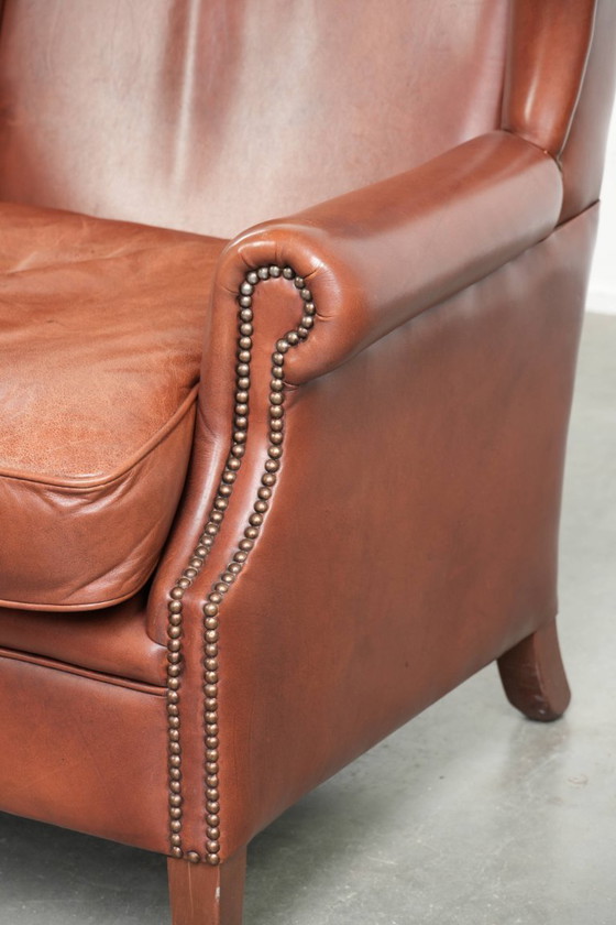 Image 1 of Comoda poltrona a orecchioni in pelle bovina color cognac in stile inglese.