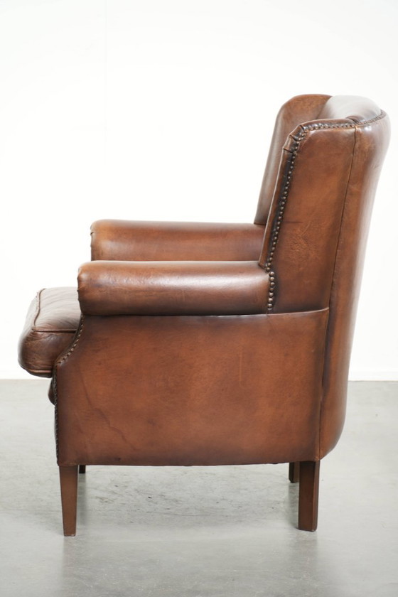 Image 1 of Precioso sillón orejero de piel de oveja marrón oscuro con un aspecto atemporal en un tamaño sutil.