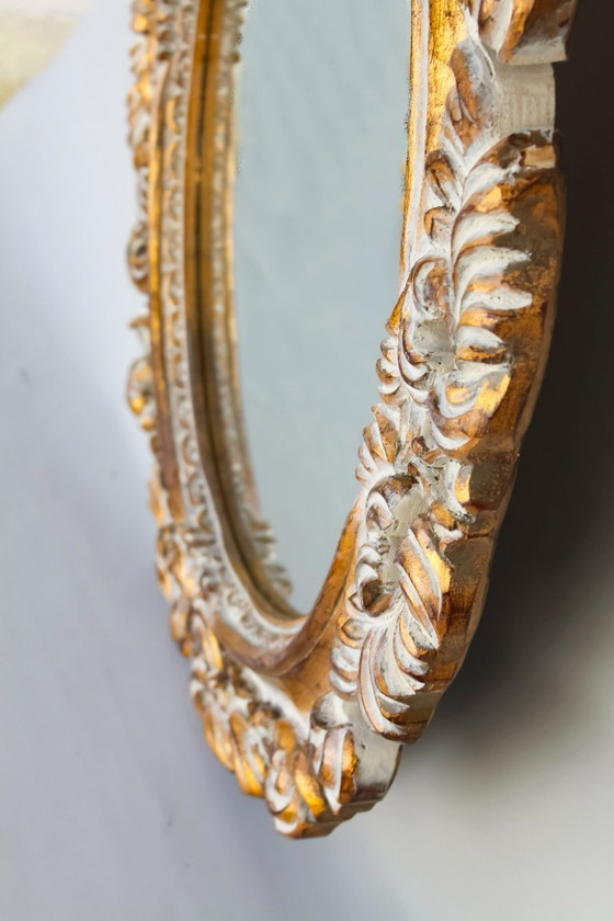 Image 1 of Oval mirror, gilded and carved from wood. Decorated and distressed with scrolls and leaves. Exclusively handmade by artisans.
