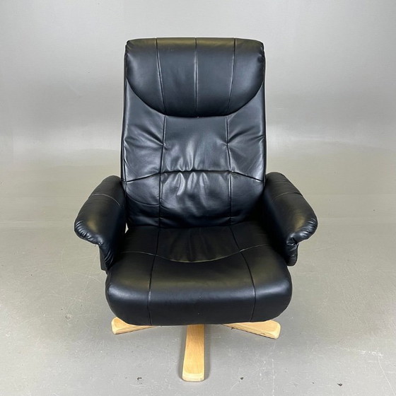 Image 1 of Two‑piece lounge set by Ekornes comprising a swivel reclining armchair and a matching footstool in black leather with a wood fra
