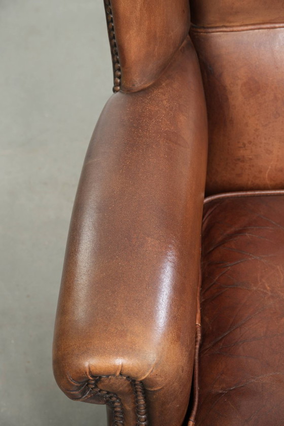 Image 1 of Precioso sillón orejero de piel de oveja marrón oscuro con un aspecto atemporal en un tamaño sutil.