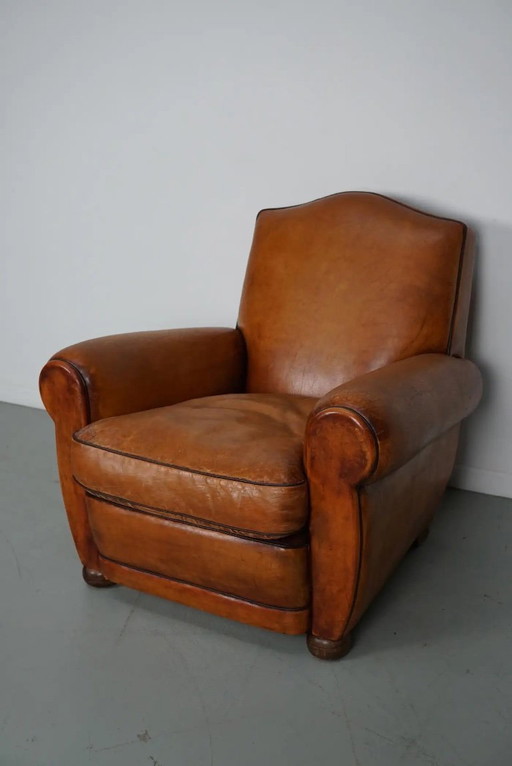 Sillón club francés vintage de cuero color coñac con respaldo en forma de bigote.